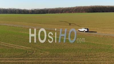 Suv Driving On A Countryside Road In A Grazing Light Among Large Fields, Video Drone Footage