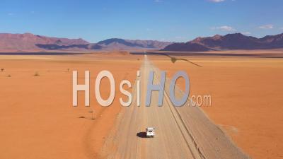 Aerial View Over A Safari Vehicle Heading Across The Flat, Barren Namib Desert In Namibia - Video Drone Footage
