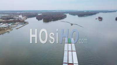 Aerial View Of A Coal Barge Pushed By Tugboat Moving Up The Mississippi River Near Burlington Iowa With Suspension Bridge Foreground - Video Drone Footage