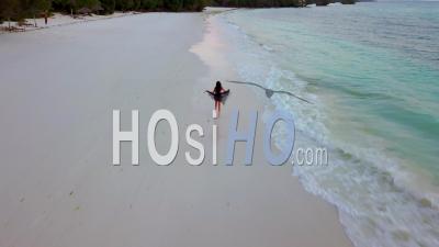 Aerial View Of A Woman Model Running Freely Along A White Sand Tropical Beach In A Flowing Dress Or Skirt.