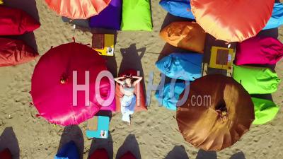 Aerial View Over A Woman Relaxing Beneath Colorful Beach Umbrellas In Sanur Or Kuta Beach On The Coast Of Bali, Indonesia - Video Drone Footage