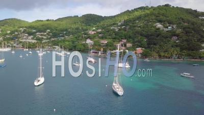 Aerial View Of A Sailboat Sailing Across The Caribbean Ocean Sea Near The Island Of St. Vincent With Rainbows And Shoreline Distant - Video Drone Footage