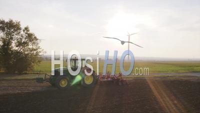 Gros Plan D'un Tracteur De Labour Au Coucher Du Soleil Avec Une éolienne En Arrière-Plan - Vidéo Drone