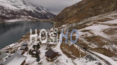 Car Driving On A Road Next To A Village Near A Lake In The Alps, Tignes, France - Video Drone Footage