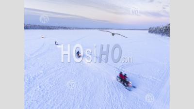 Aerial Drone Photo Of Snow Mobiles On A Snowmobiling Adventure On A Snow Covered Lake In Winter At Finnish Lapland, Finland