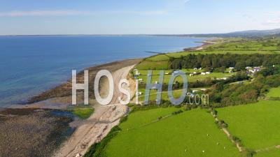 Aerial Drone Shot Of Idyllic Green Farmland And Fields On Coast Of Wales On Sunny Summer Day With Low Tide Ocean And Beach
