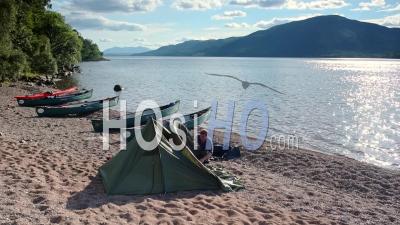 Man Setting Up A Tent Near The Boats On The Sandy Shore Of Caledonian Canal, Loch Ness, Scottish Highlands In Scotland On A Summer Day - Timelapse