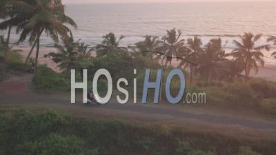 Motorcycle Rider Driving On The Road With Palm Trees In Varkala, India At Sunset Scenery By The Sea - Aerial Drone Shot
