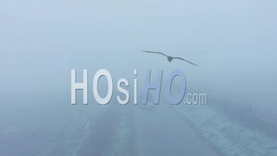 Aerial Drone Video Of Car Driving In Misty Thick Foggy, Bad And Dangerous Driving Conditions On A Rural Countryside Road, 4 Wheel Drive With Trailer Driving Past Fields In England In Mist And Fog