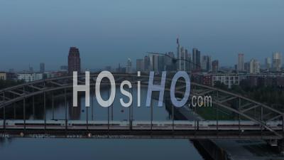 Frankfurt Am Main Skyline At Blue Hour Early Morning Over Main River With Passanger Train Passing Bridge, Aerial High Angle Slow Forward - Video Drone Footage