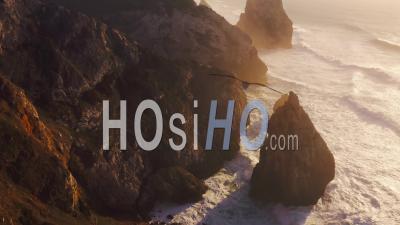 Aerial Drone View Of Cliffs And Dramatic Portugal Coast Scenery At Lisbon, Atlantic Ocean And Coastal Waves Landscape Of Rock Formations, Rocks And Rocky Coastline, Europe With Orange Sunset Light