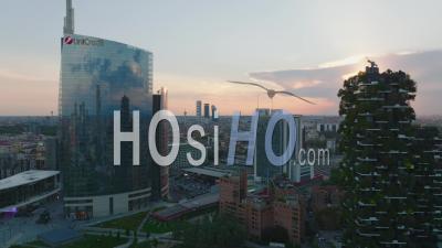 Forwards Fly Around Modern High Rise Office Buildings With Glossy Glass Facade. Revealing Transport Terminal And Cityscape At Sunset. Milano, Italy. - Video Drone Footage