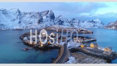 A Town On The Lofoten Islands, Norway Is Seen With Snow-Covered Mountains In The Distance - Video Drone Footage