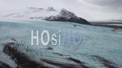 Aerial Of A Glacier Frozen By A Snow-Covered Mountain Range In Iceland - Video Drone Footage