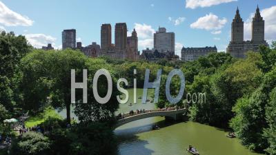 Tourists Are Seen Walking On Bow Bridge And Rowing Boats On The Lake Under It In Central Park, New York - Video Drone Footage