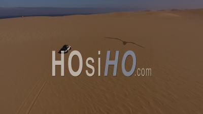 White Pick Up Driving To The Atlantic Ocean On Sand Dune In The Namib Desert, Followed By Drone